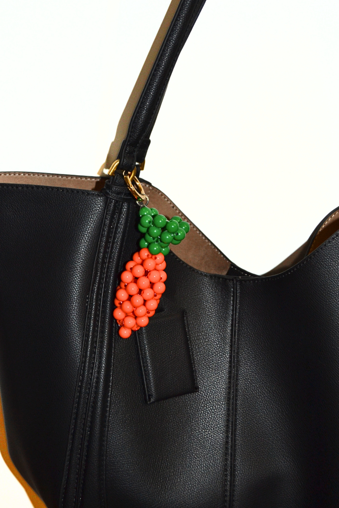 Black handbag with a decorative charm featuring a carrot made of beads on a white background