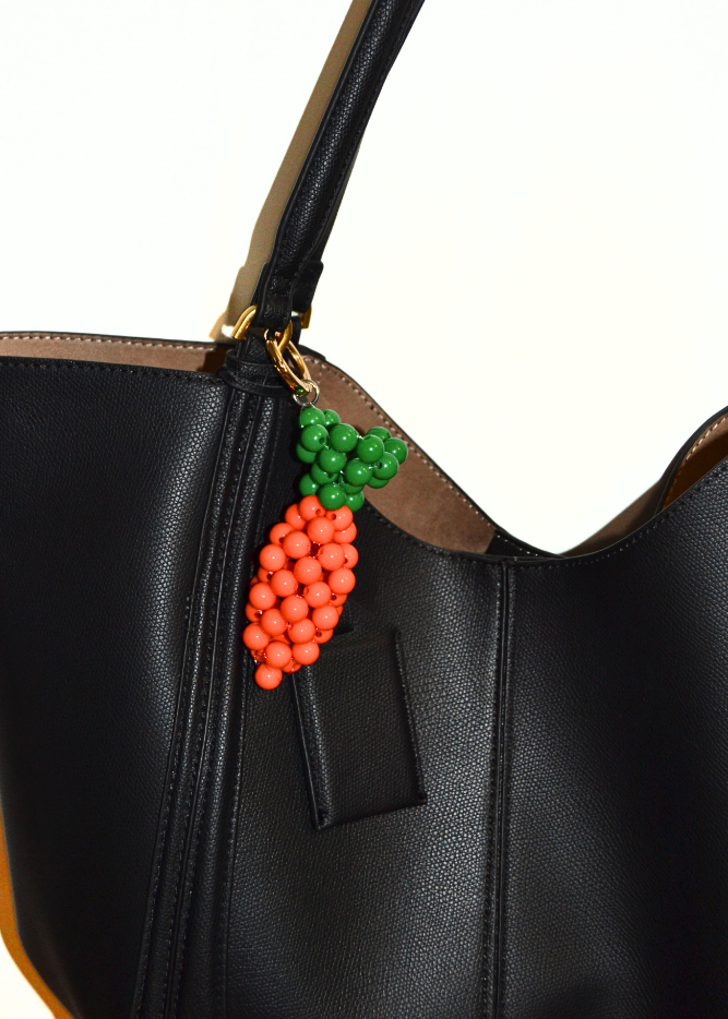 Black handbag with a decorative charm featuring a carrot made of beads on a white background