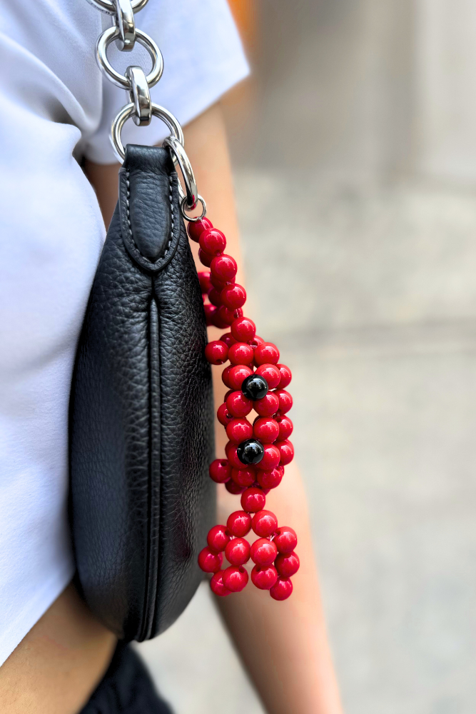 Black clutch with a red beaded charm held by a person wearing a white shirt.