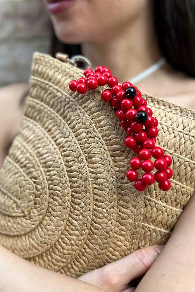 Straw clutch with a red beaded accessory held by a person
