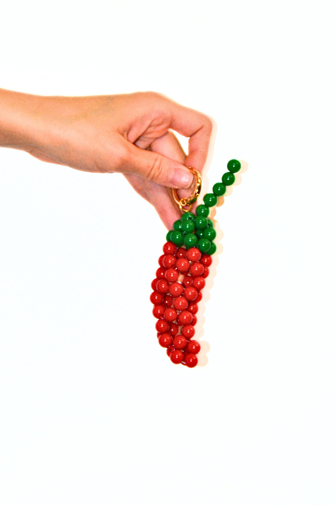 Hand holding a beaded carrot charm on a white background