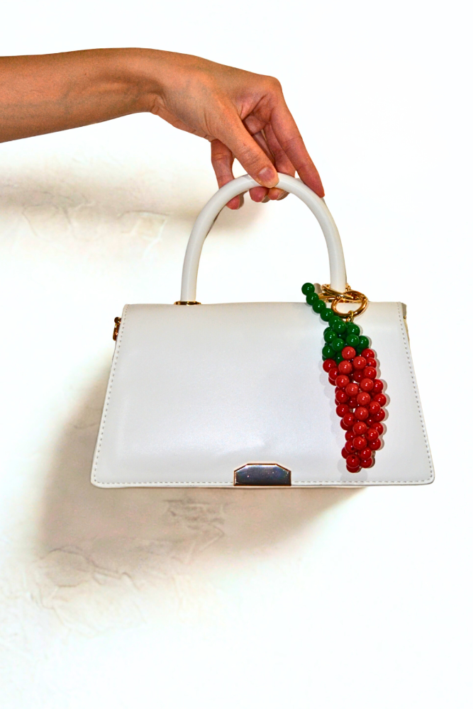 White handbag with red and green bead design held by a hand on a white background