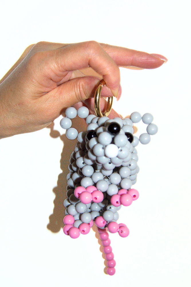 Hand holding a keychain shaped like a mouse with gray, pink, and black beads on a white background