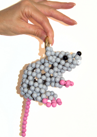 Hand holding a beaded mouse toy with gray, pink, and black beads on a white background