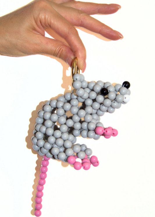Hand holding a beaded mouse toy with gray, pink, and black beads on a white background