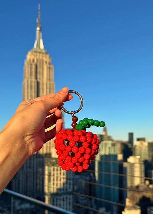 Hand holding a red beaded apple keychain with a city skyline in the background