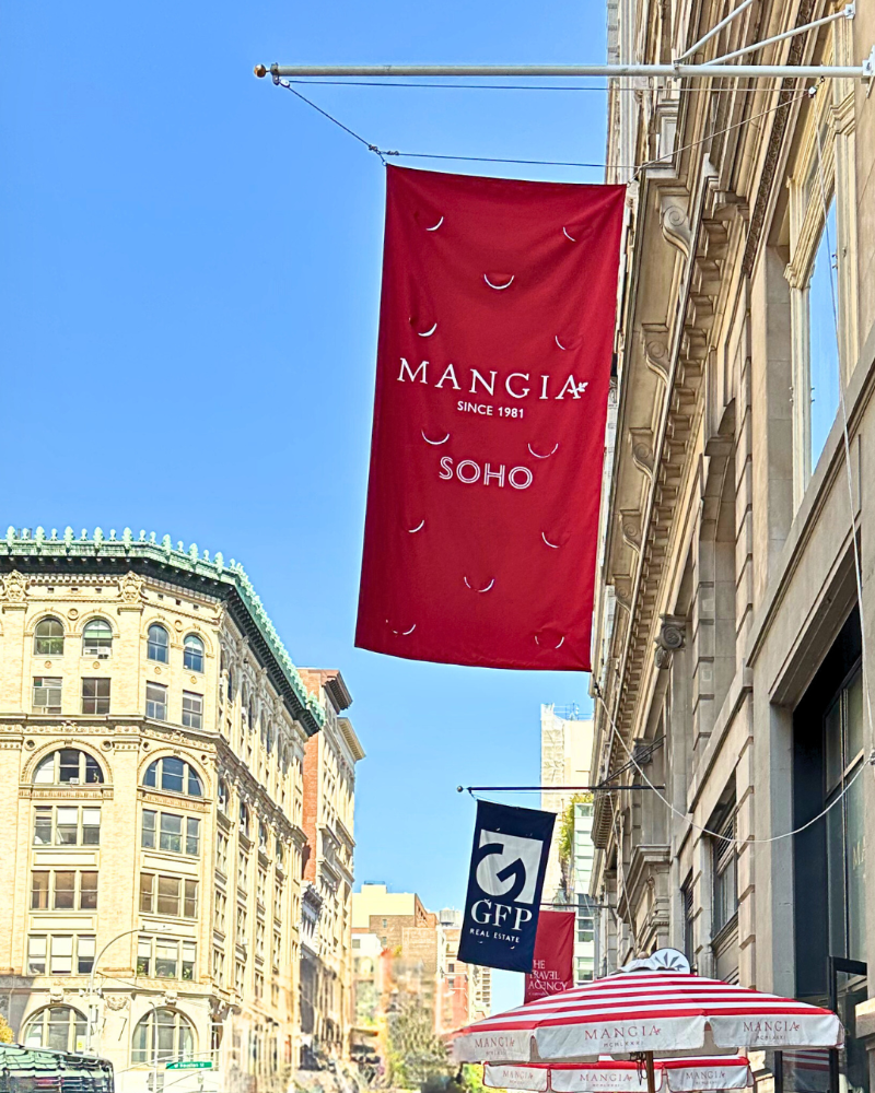Red Mangia SoHo banner hanging from a building with a clear blue sky.
